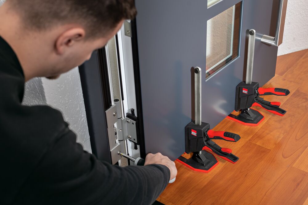 Одноручный монтажный инструмент BEYCEPS поднимает входную дверь, техник правильно регулирует дверь с помощью отвертки